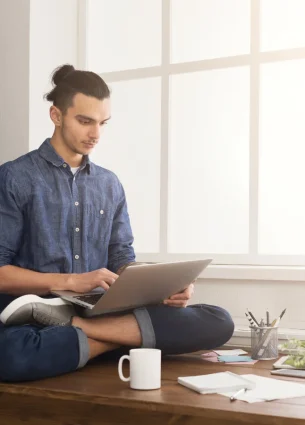 Man sitting cross-legged on the floor, working on a laptop, symbolizing improved flexibility and relaxation from corporate massage therapy