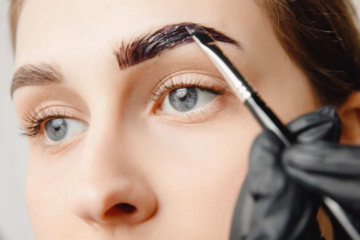 Close-up of a beautician applying brow tint for a custom eyebrow transformation.