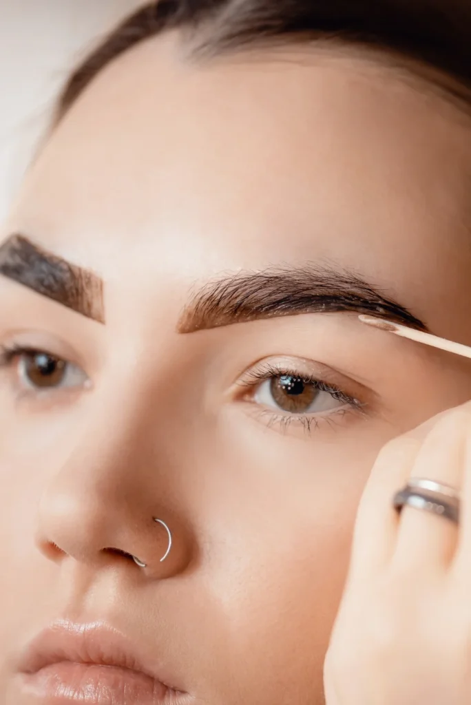 Close-up of a beautician applying eyebrow tint to a client for a fuller and more defined brow look.