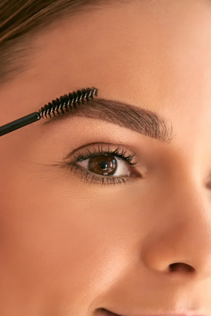 Close-up of a woman brushing her eyebrows after a Brow Henna treatment, showing well-defined and fuller brows for a natural, long-lasting look