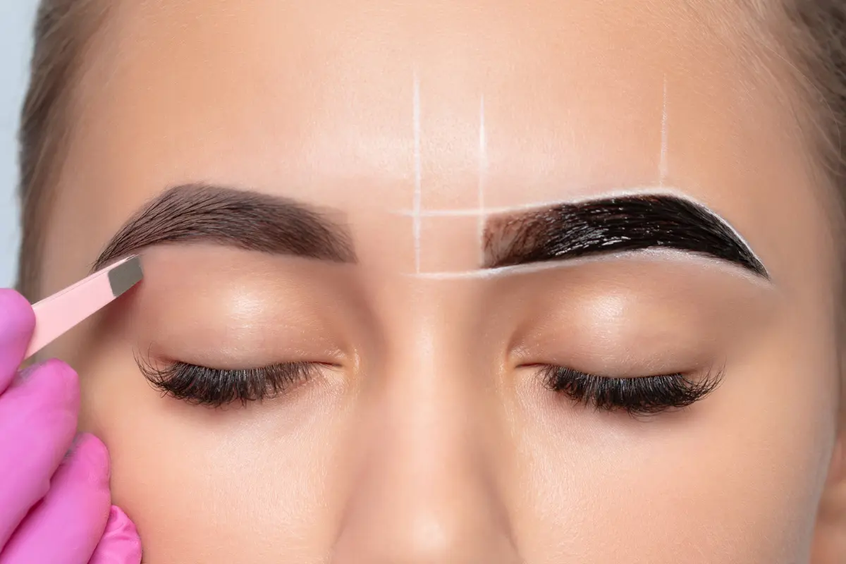 Close-up of a beauty technician shaping eyebrows with henna, showing the process of contouring for a fuller, sculpted brow look