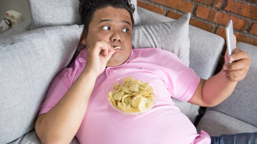 a man lying on a couch eating potato chips